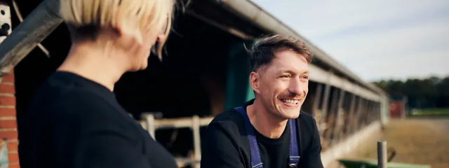 Zwei Personen unterhalten sich neben einem Kuhstall Zwei Personen unterhalten sich neben einem Kuhstall